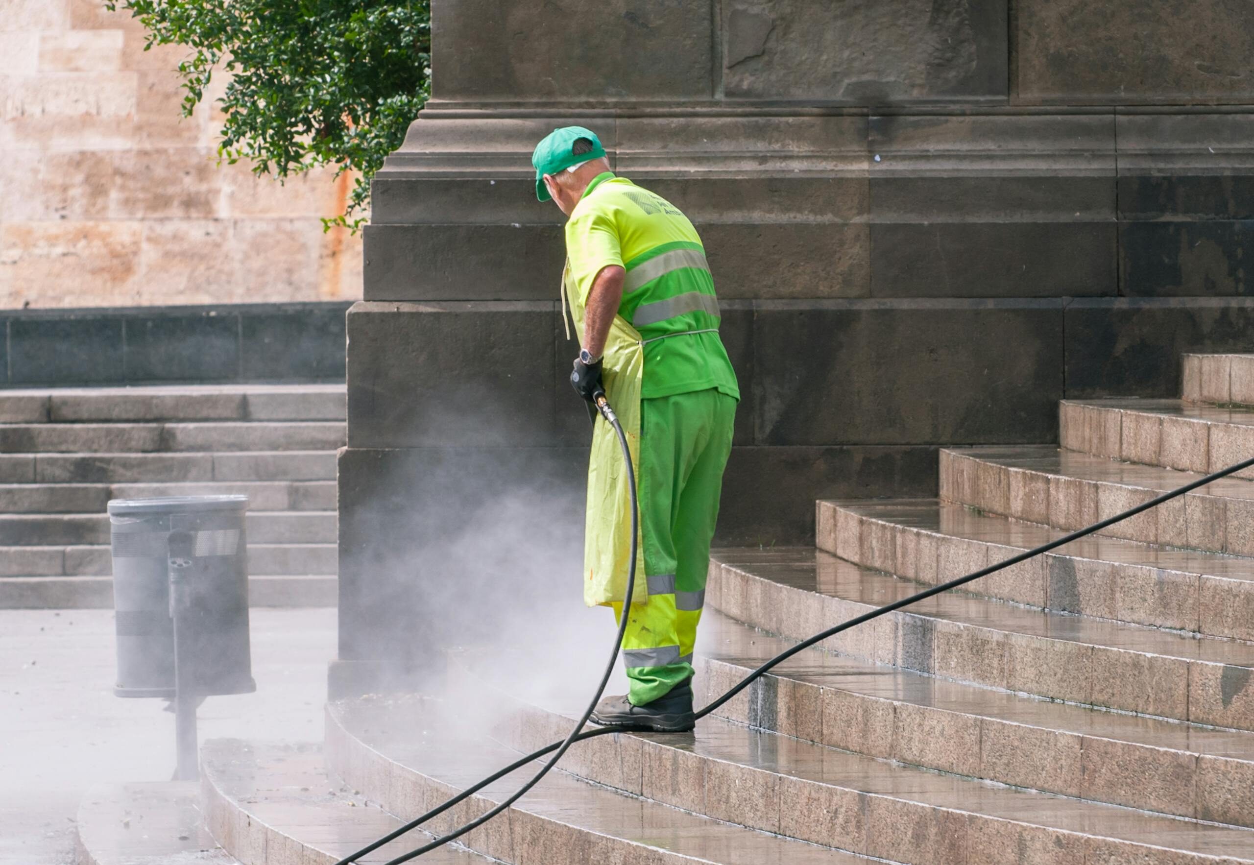 A street worker pressure washes stone stairs in a public park, ensuring cleanliness and safety.